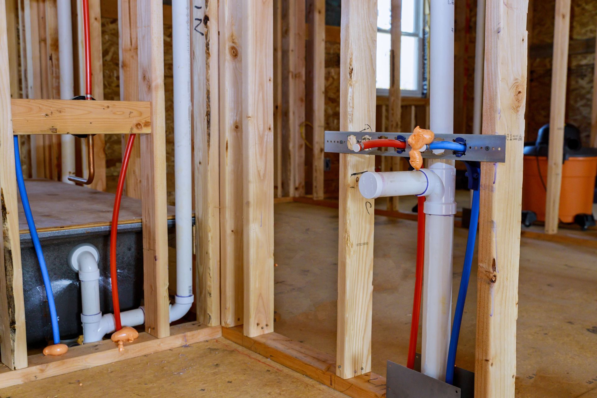 Unfinished bathroom framing with exposed plumbing pipes and a wall-mounted shower valve.