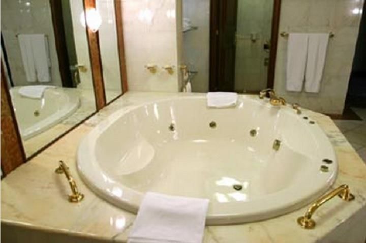 Luxurious bathroom with a large round jetted bathtub and gold fixtures, towels hanging nearby.