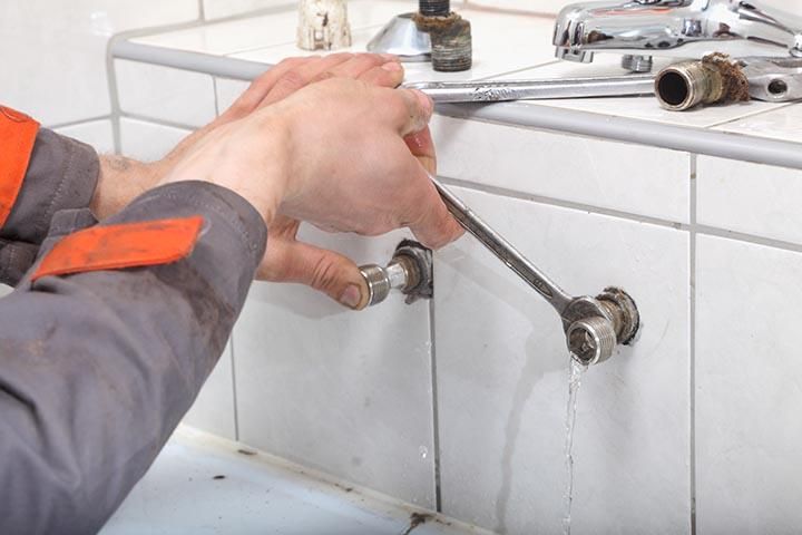 Hands tightening a faucet under a white tiled sink area