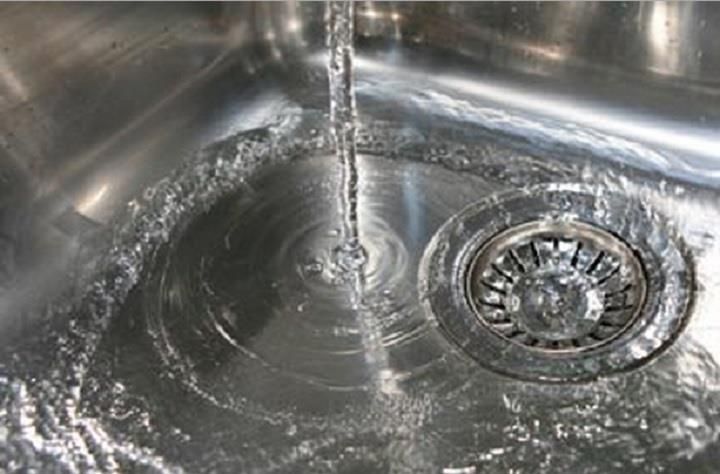 Water running into a stainless steel kitchen sink with a drain strainer.