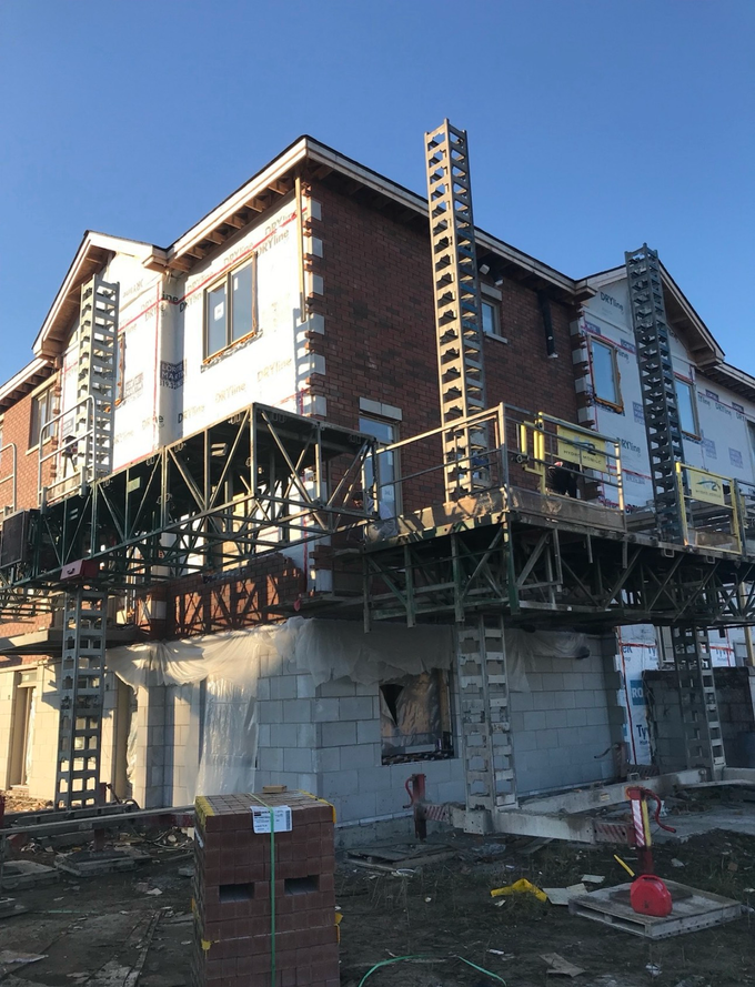 Maison en construction avec échafaudages et murs de briques apparentes par une journée ensoleillée