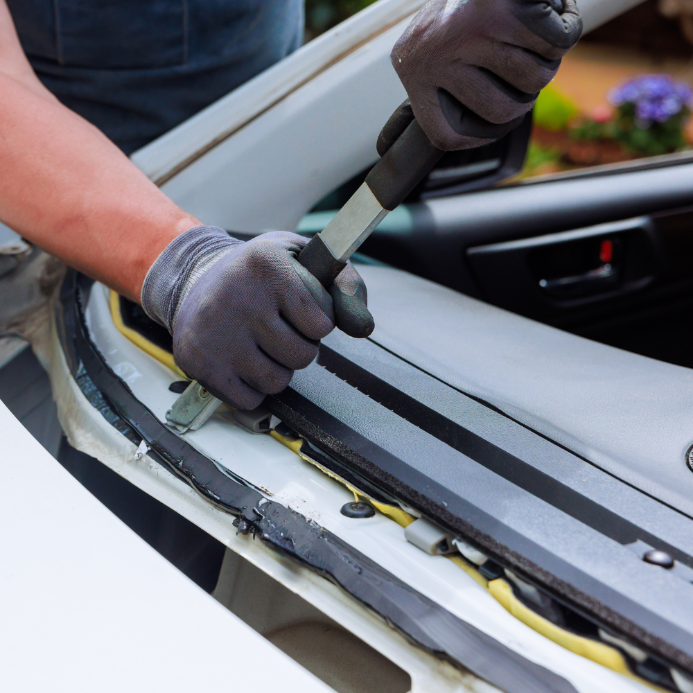 Gloved hands applying adhesive along a car windshield frame during repair