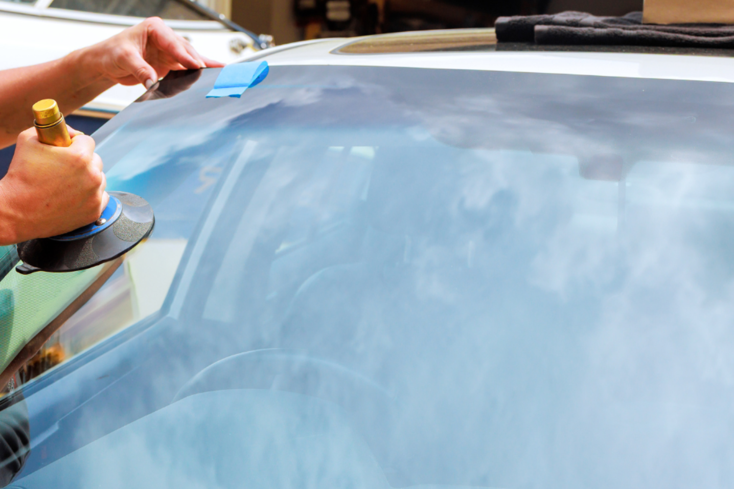 Hands applying a blue tint film to a car windshield with a squeegee
