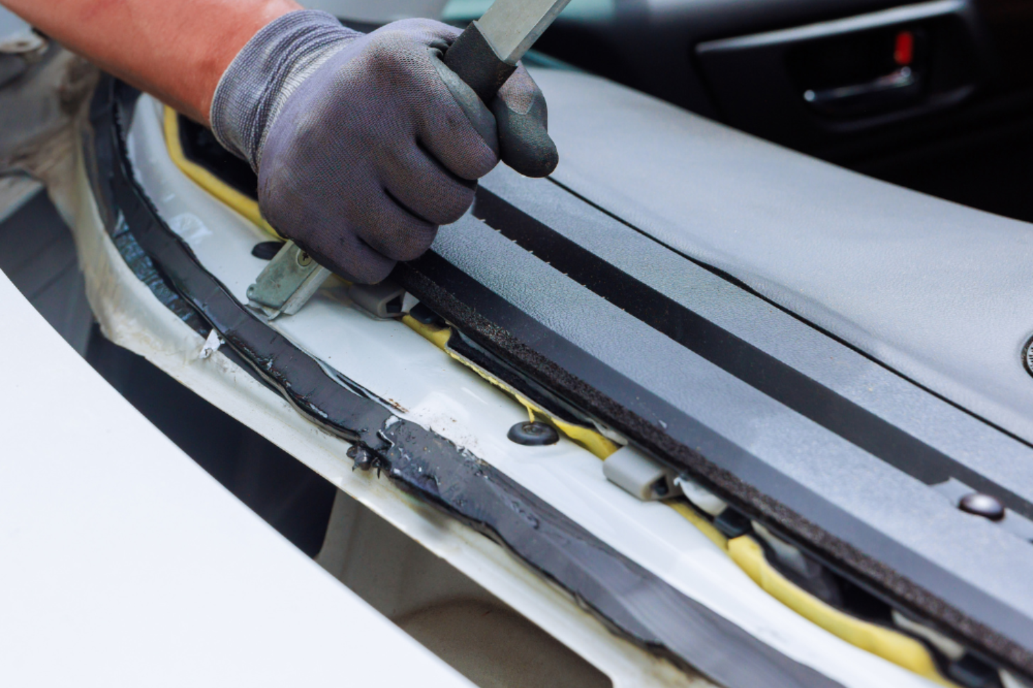 Gloved hands installing trim on a car windshield edge