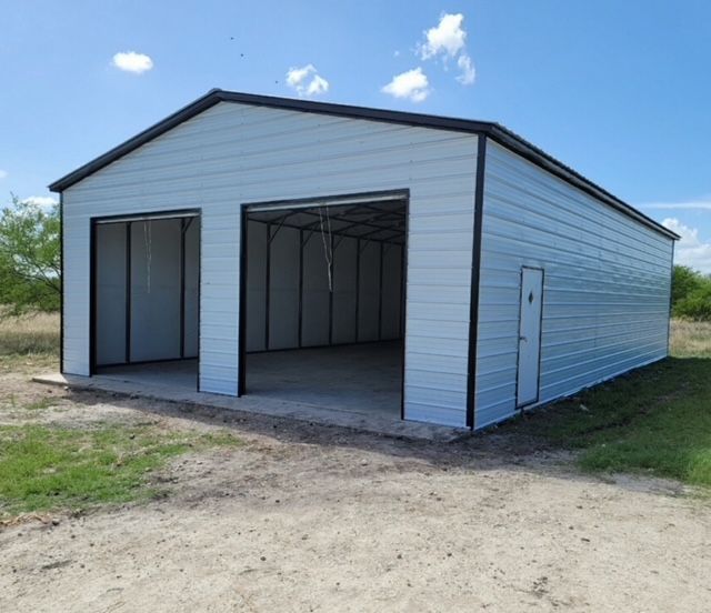 Metal building with open front bays and white siding on a dirt lot under a blue sky