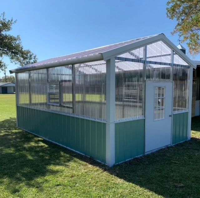 Small green-and-white enclosed shed with clear panels and a white door on a grassy lawn
