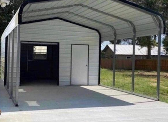 Metal carport attached to a small white shed with a concrete floor and open sides in a yard
