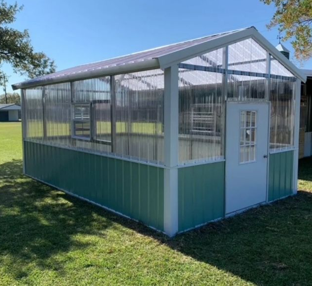 Small greenhouse with clear panels, teal lower walls, and a white door on a grassy lawn.