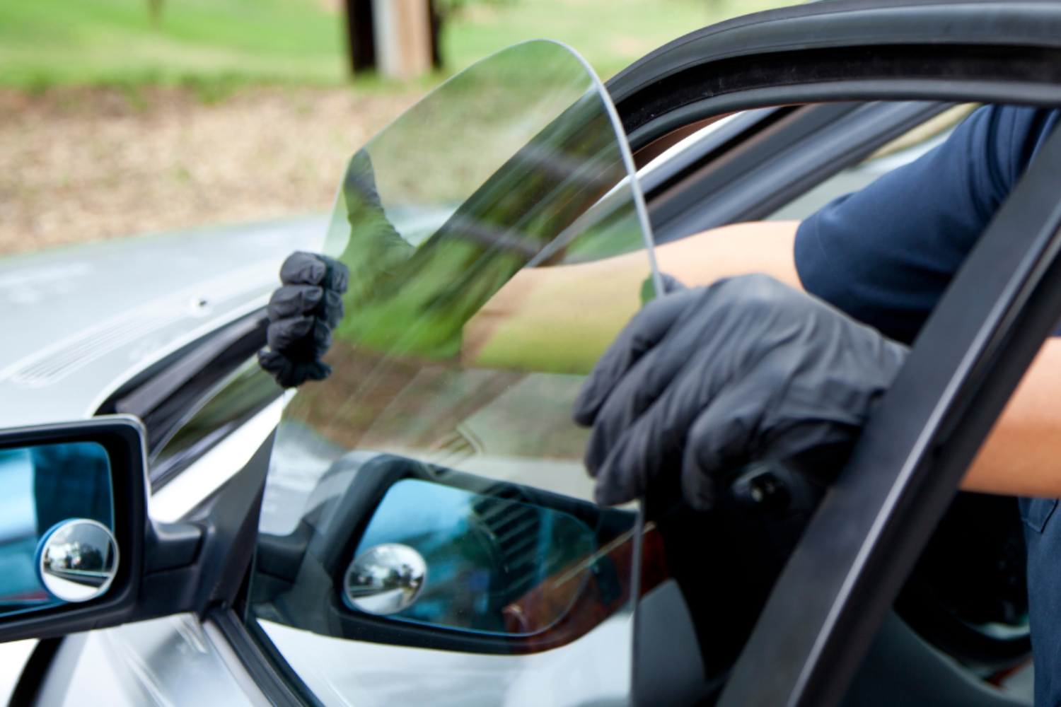 Gloved hands installing a car windshield in a blue vehicle outdoors