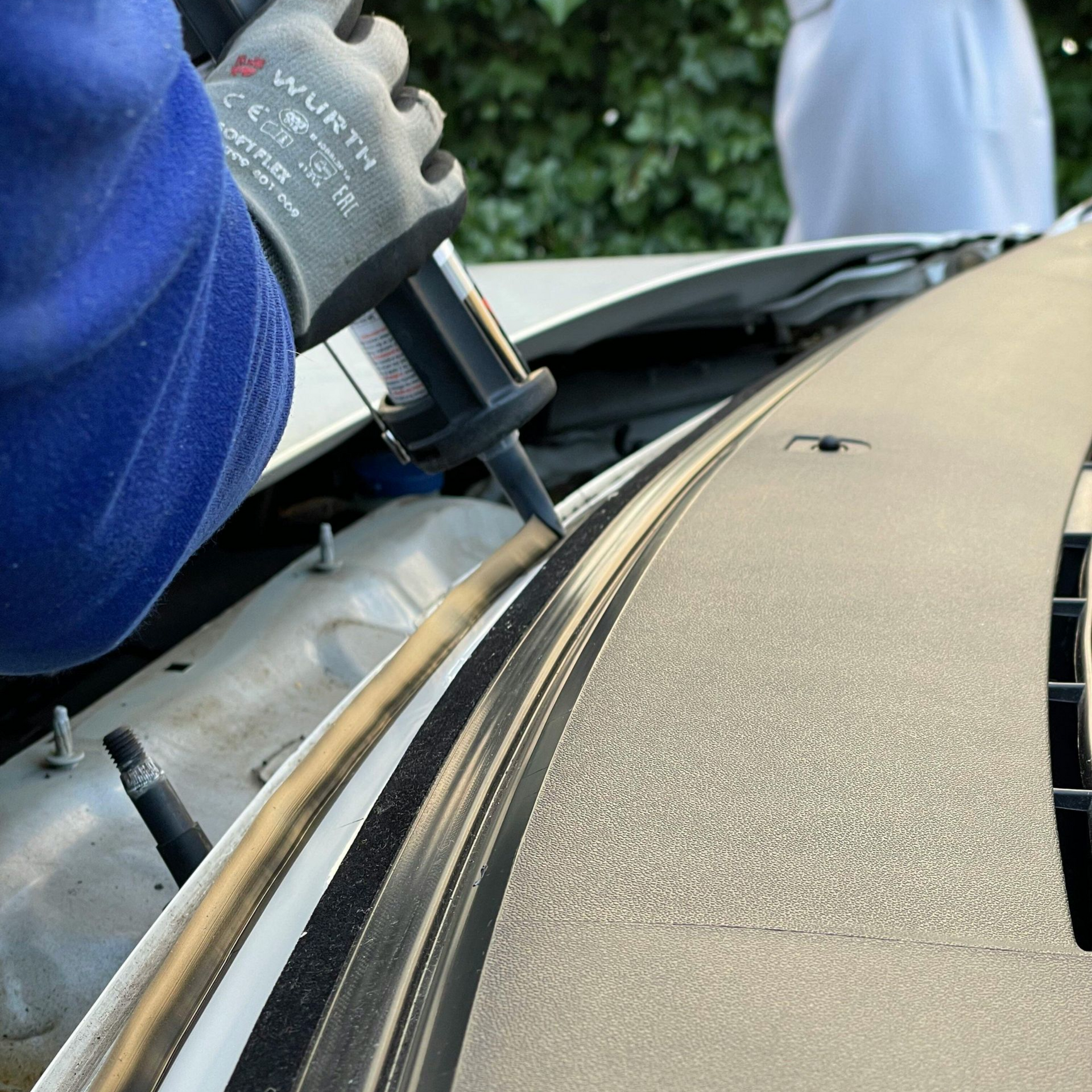 Worker using a power tool to remove or install trim on a car hood edge
