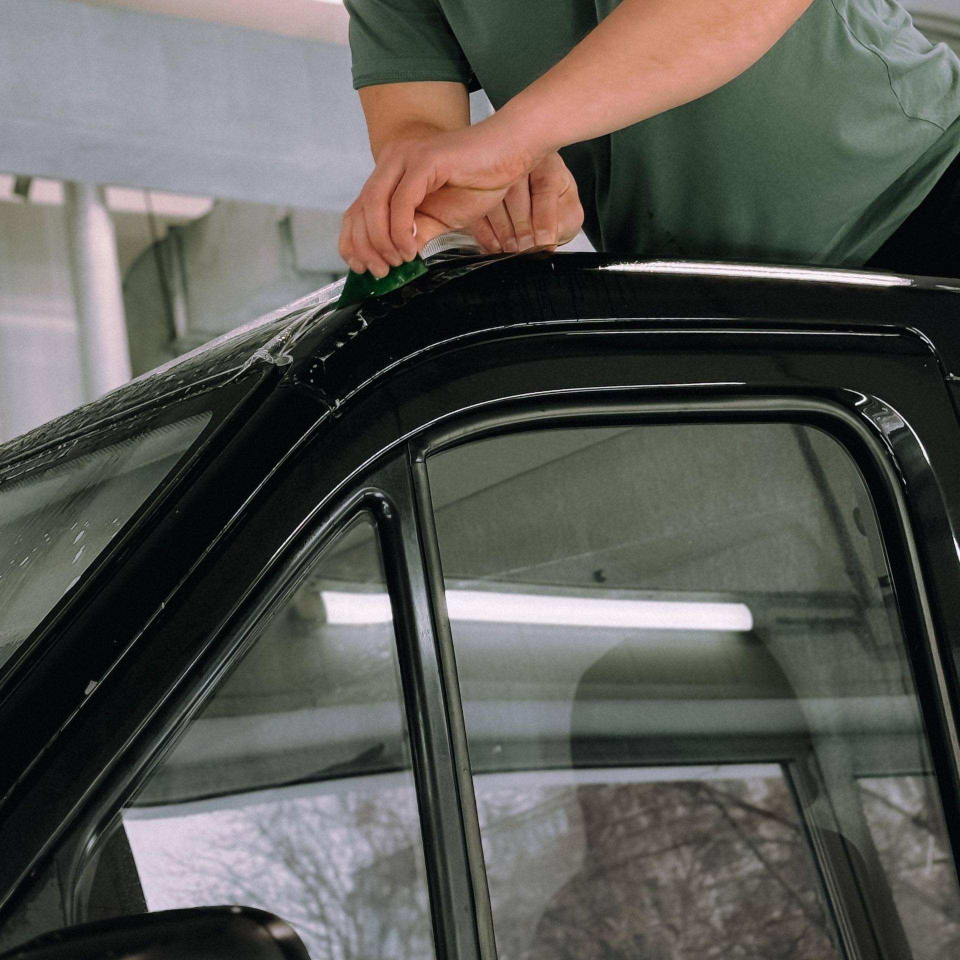 Hands polishing the roof of a black car in a garage