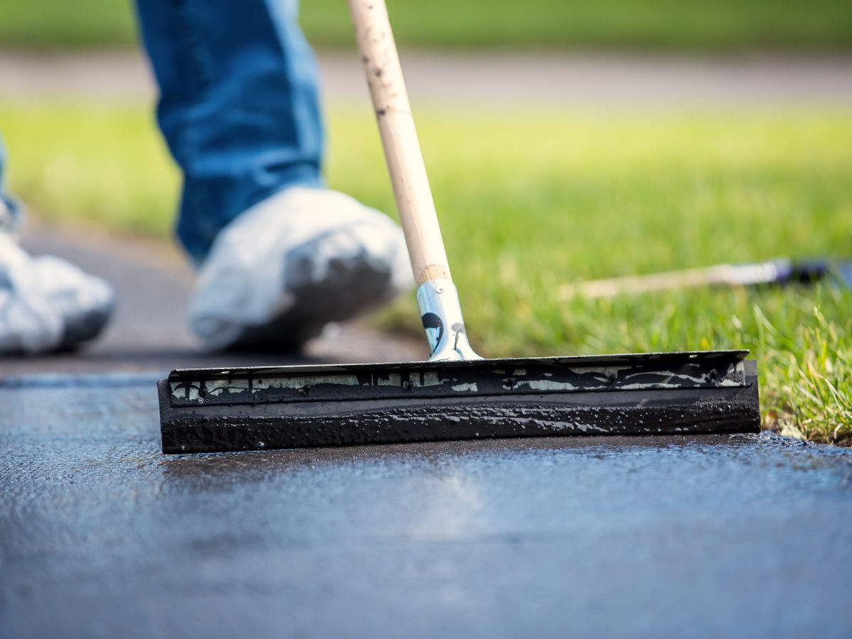 Person spreading black coating on pavement with a squeegee outdoors