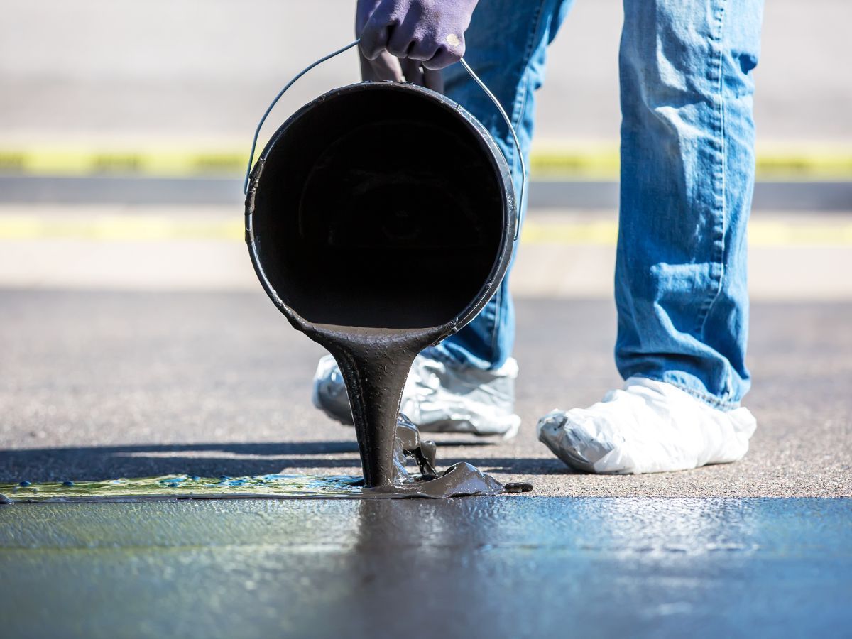 Worker pouring black asphalt from a bucket onto a road surface