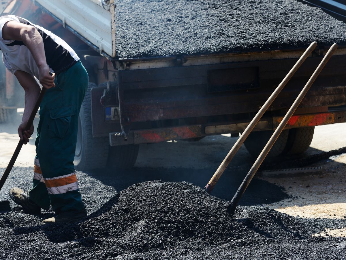 Workers spreading fresh asphalt beside a road paving truck