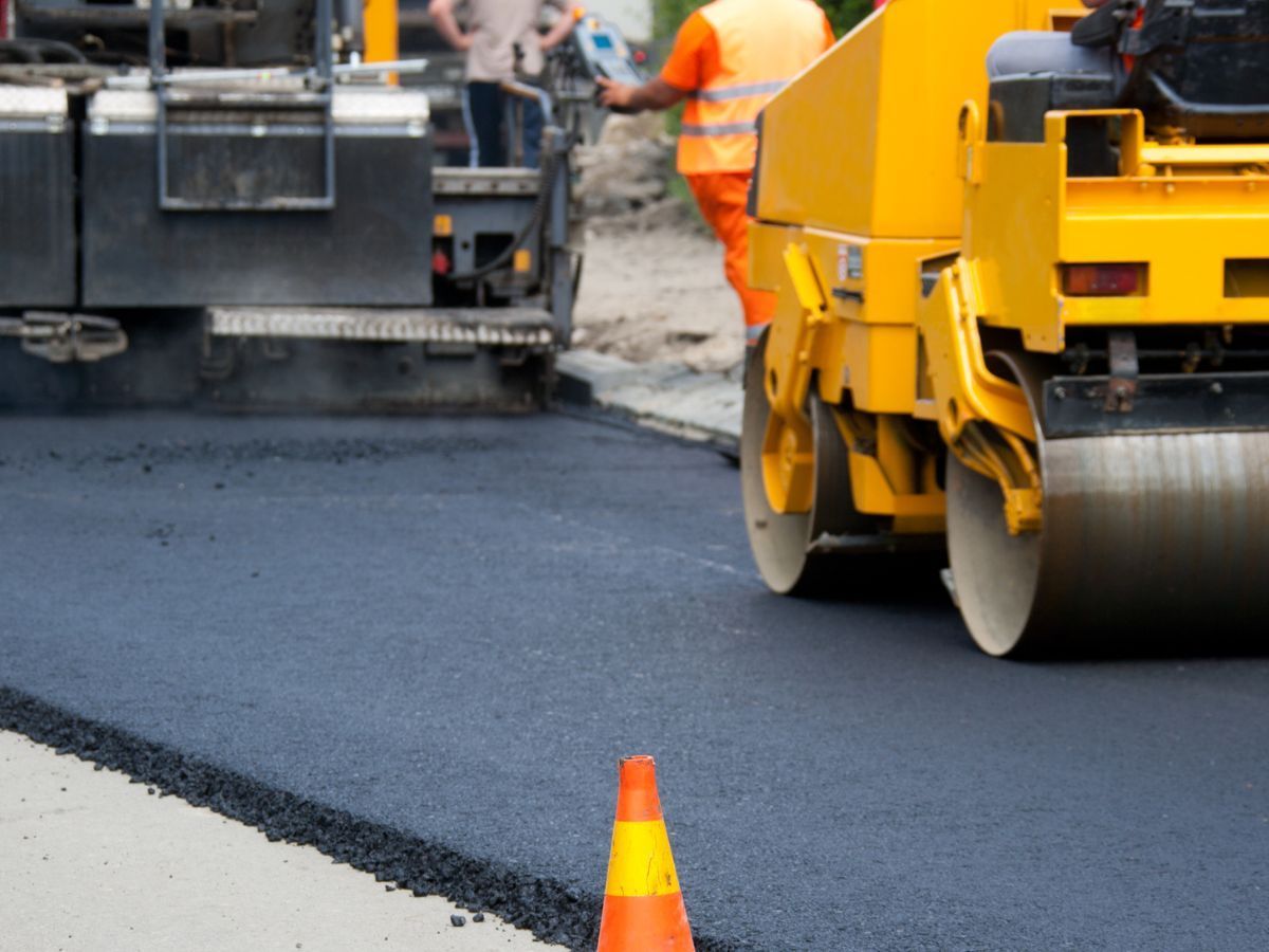 Road paving machine laying fresh black asphalt with orange safety cones nearby