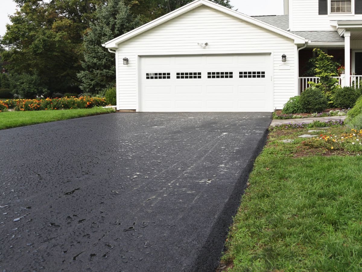 White garage with dark asphalt driveway and green lawn in front of a house