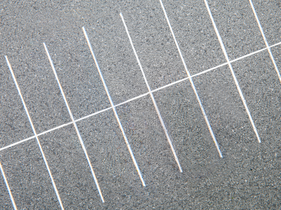 White parking lot lines on gray asphalt, viewed diagonally close-up.