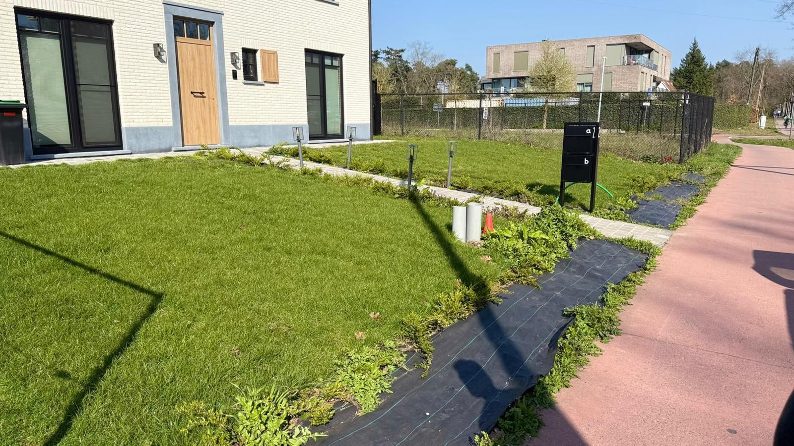 Een lichtgekleurd huis met een keurig onderhouden gazon aan de voorkant, een stukje groenbemesting en een roze stoep in de buurt.