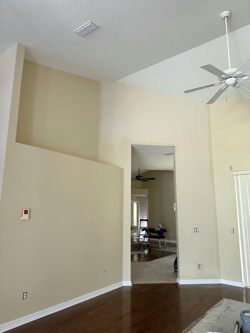 A high-ceilinged room with tan walls, white trim, and a dark wood floor.  A door leads to another room.