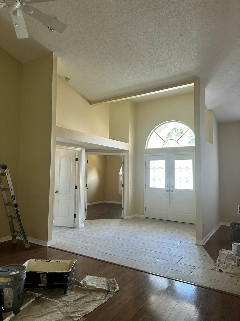 Interior view of a light-colored room with tall ceilings, arched doorway, and double doors.