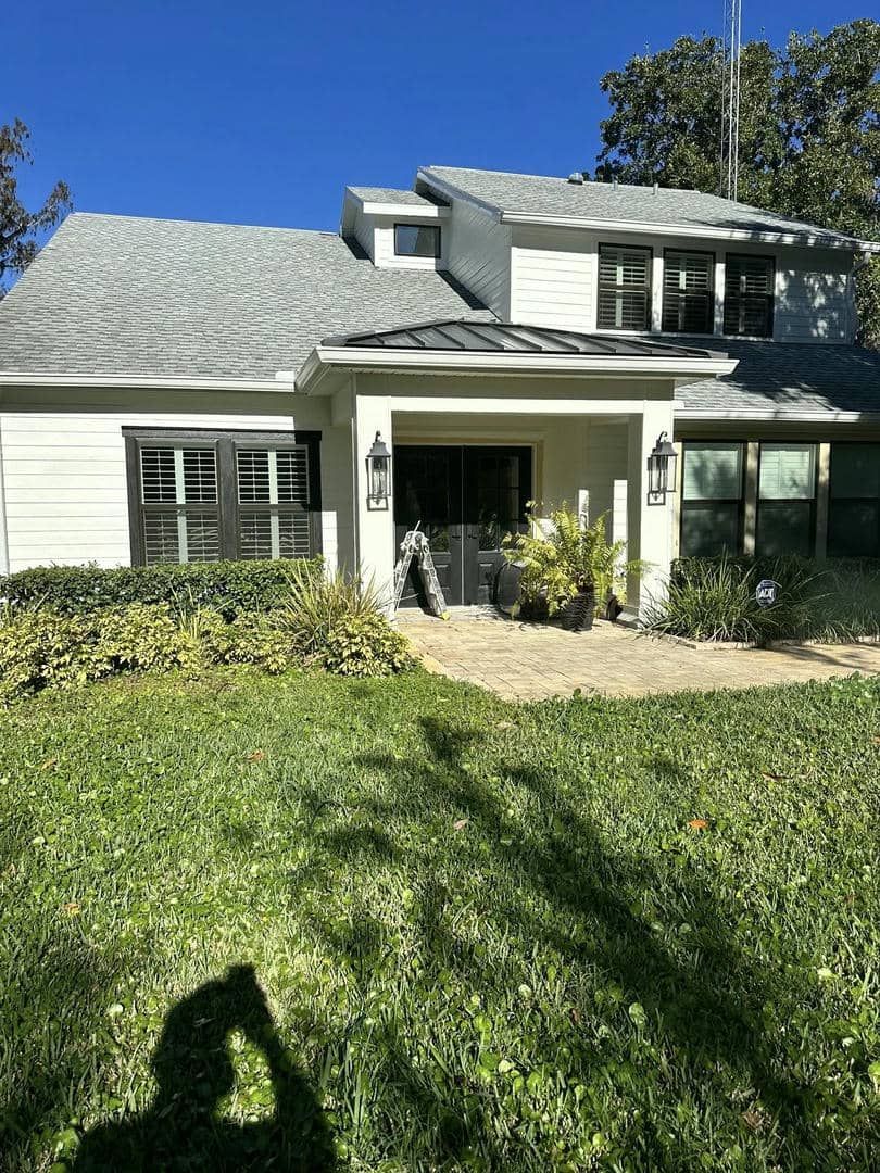 White house with gray roof, black trim. Green lawn and foliage in front.