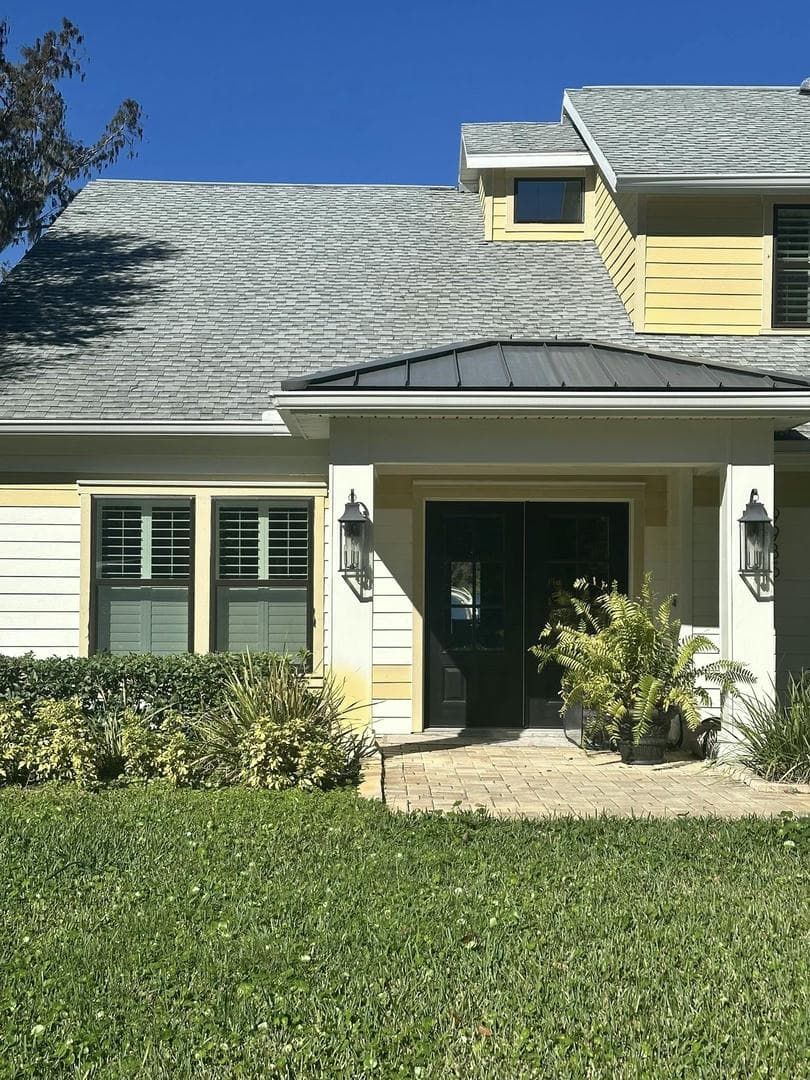 House exterior with yellow siding, gray roof, dark front door, and green lawn.