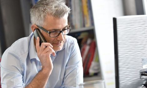A man is talking on a cell phone while sitting in front of a computer.