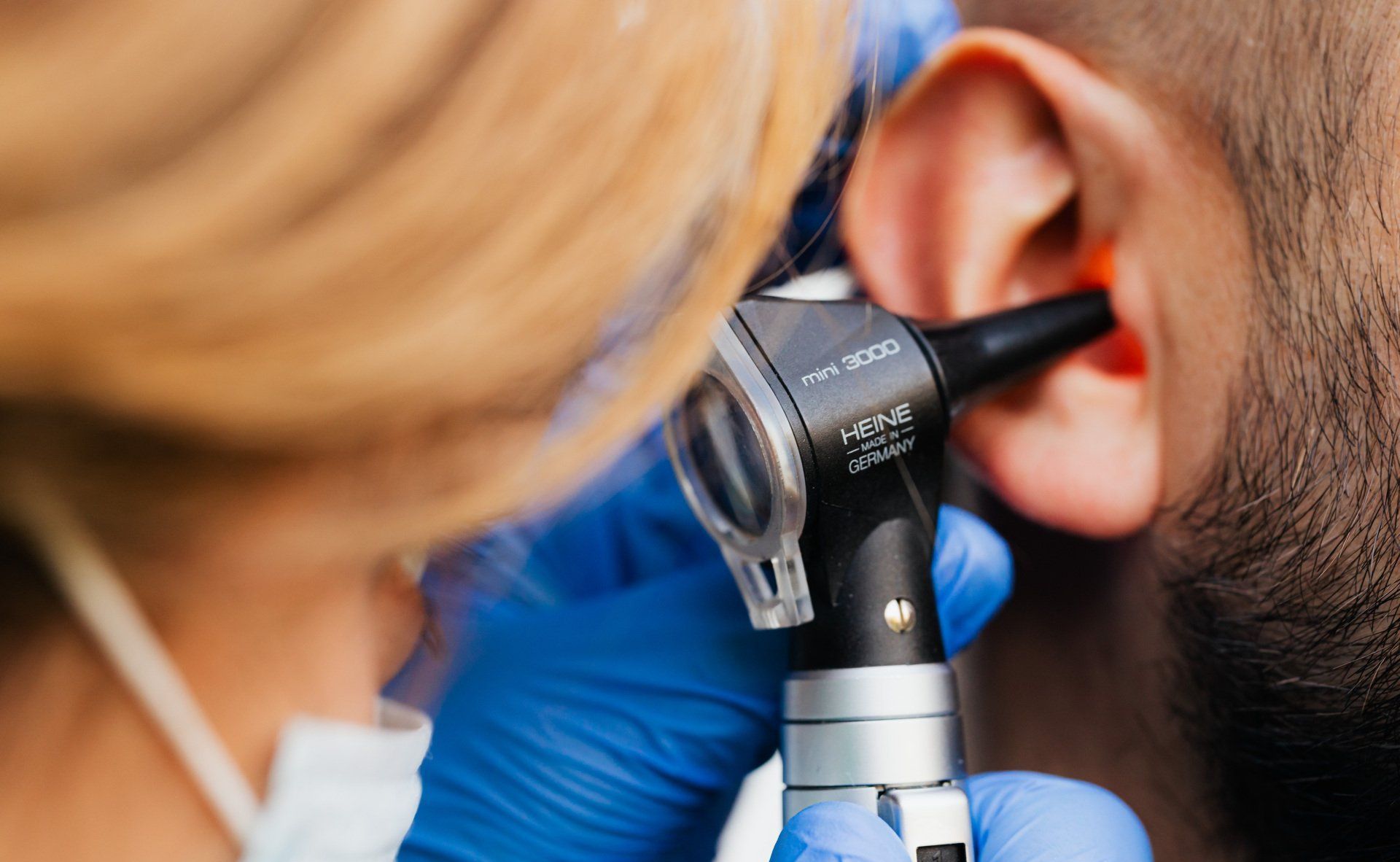 A woman is examining a man 's ear with an otoscope.