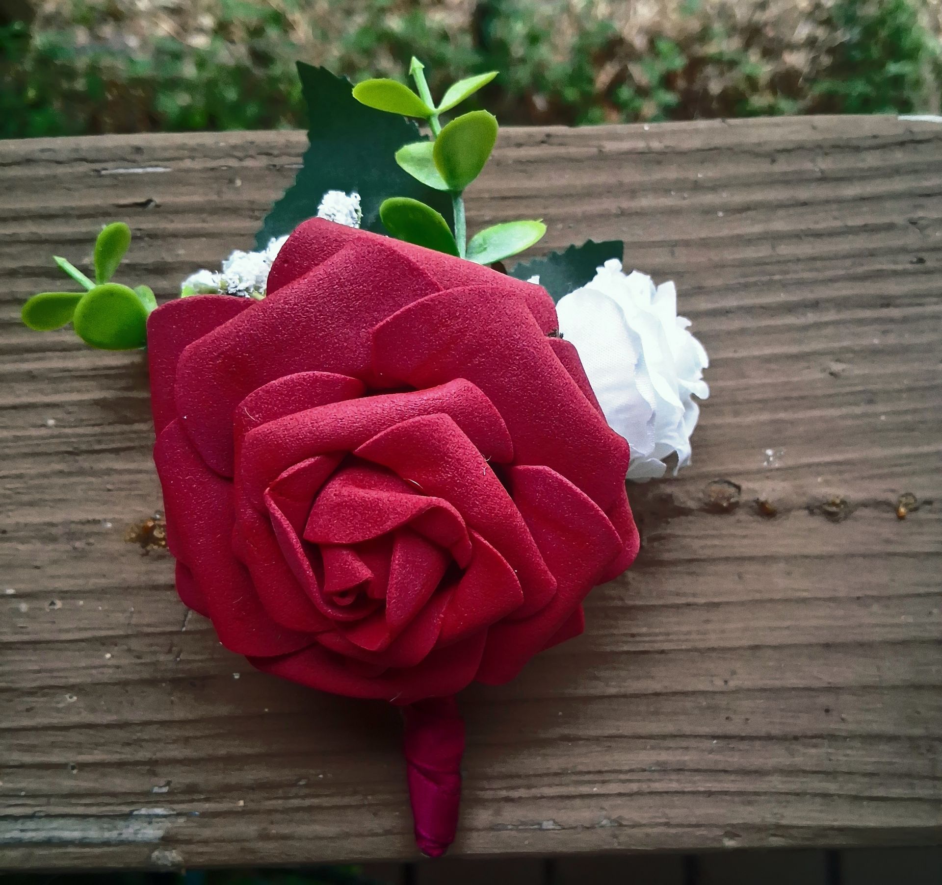 Red rose with white flowers and green leaves on weathered wooden boards.
