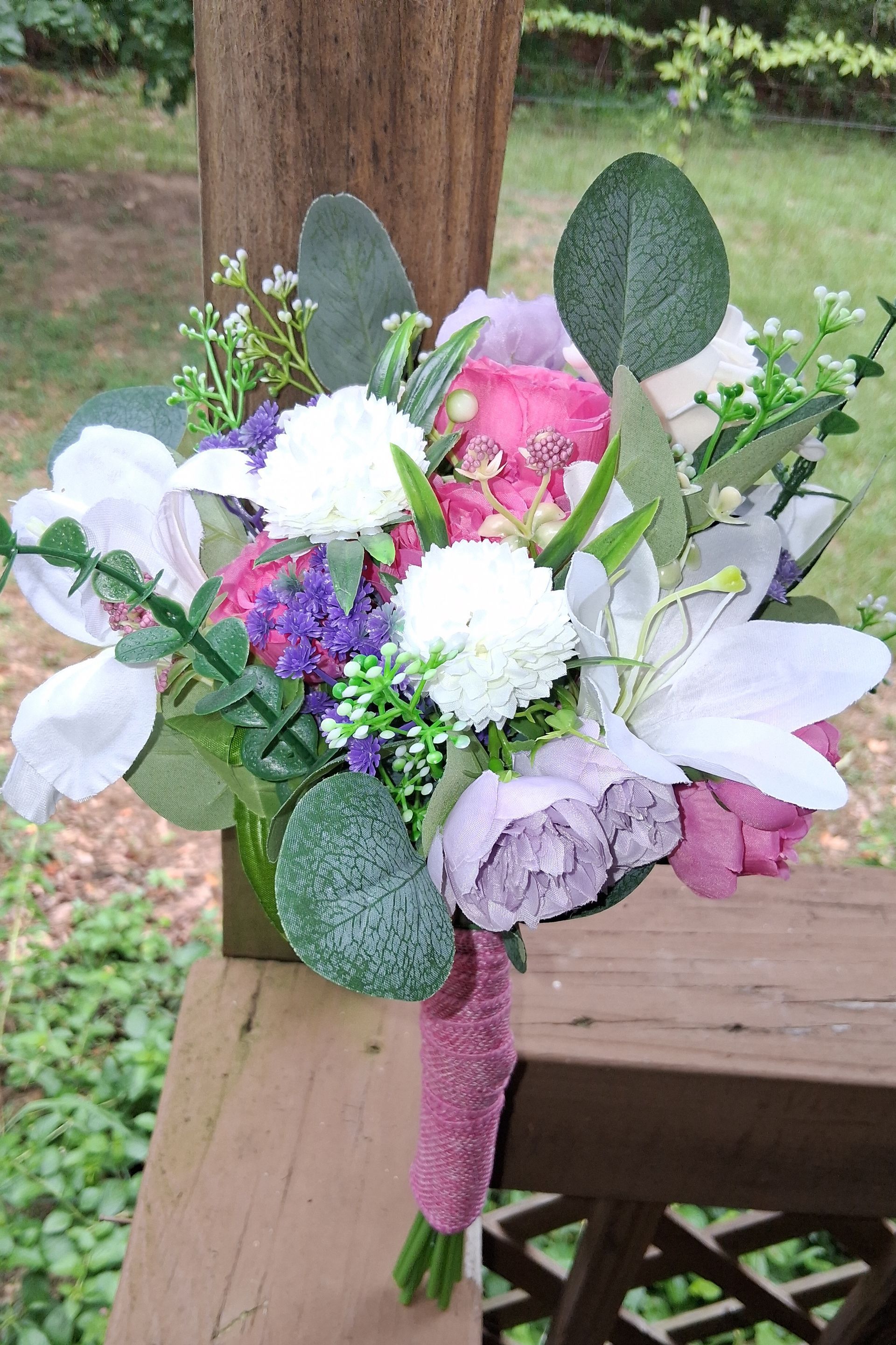 Bouquet of pink, white, and purple flowers with green leaves on a wooden deck outdoors