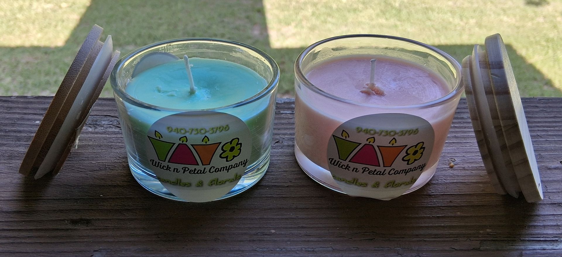 Two scented candles, blue and pink, in glass jars on a wooden surface with stacked coasters on both sides