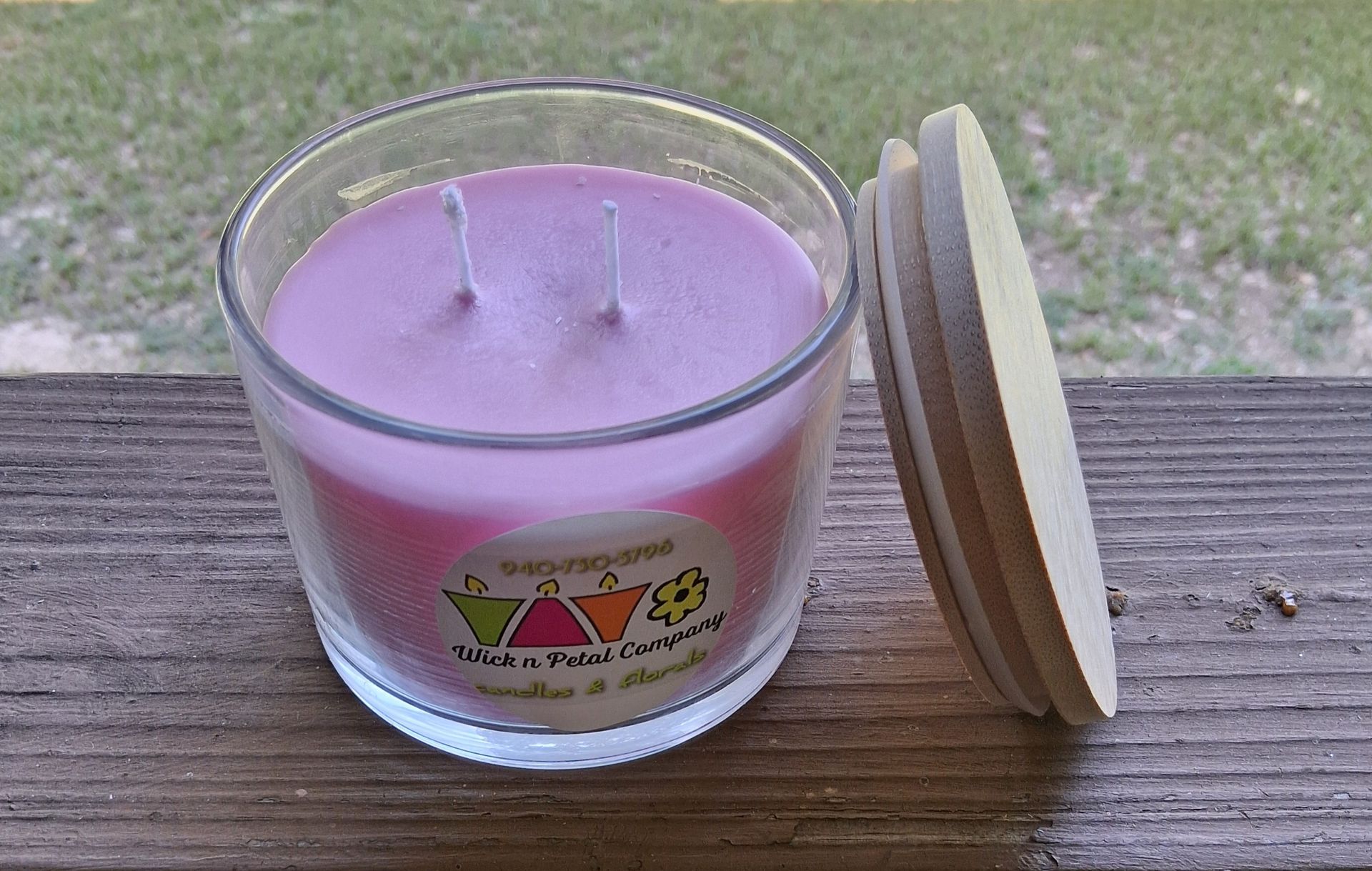 Lavender candle in a glass jar with a wooden lid on a deck railing outdoors