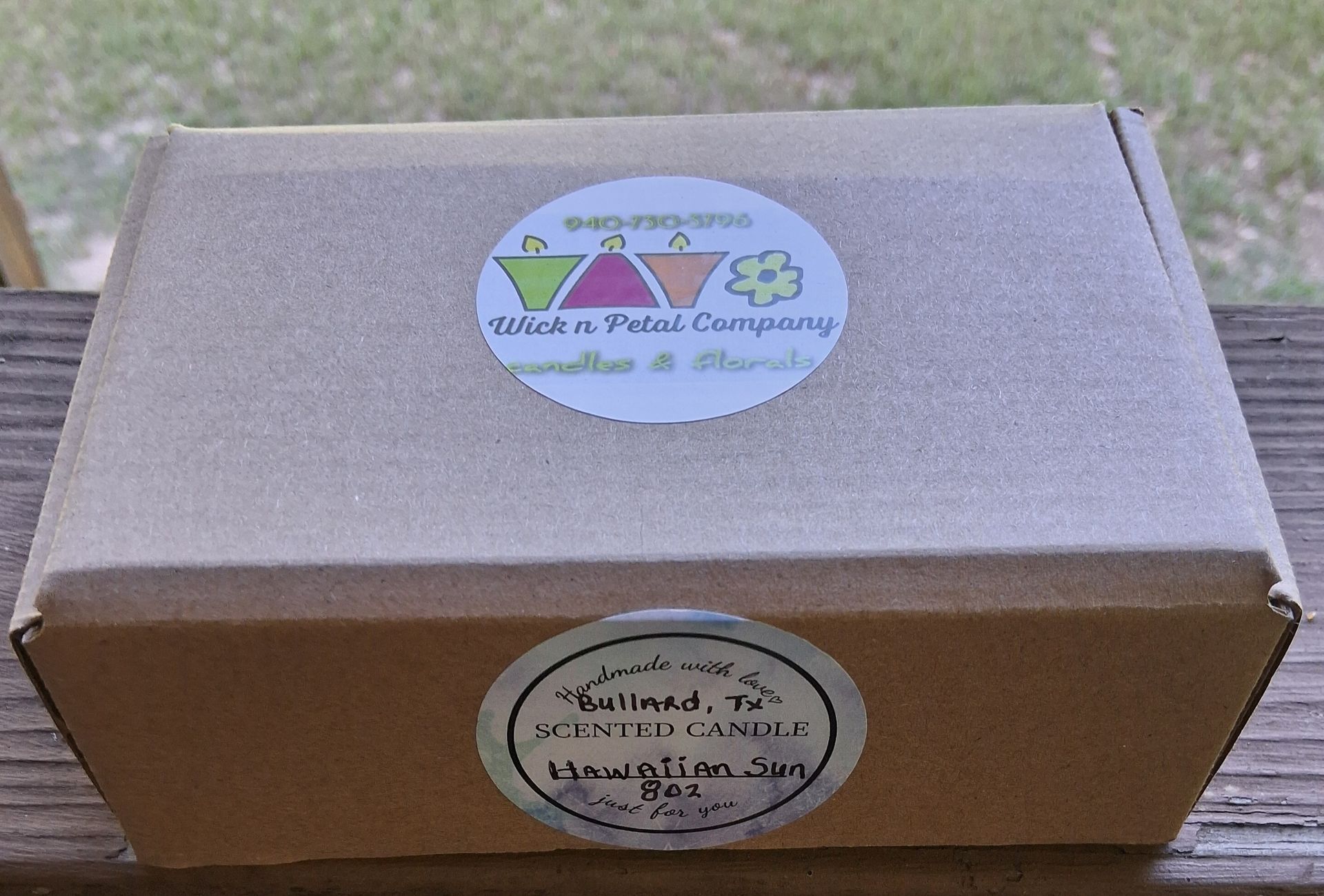 Small brown cardboard box with two round stickers on a wooden surface outdoors.