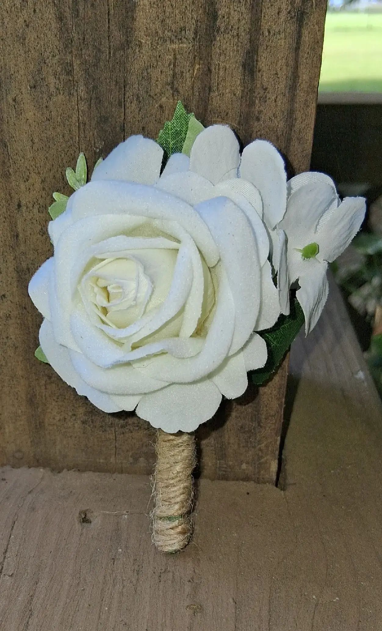 White rose bouquet with green accents wrapped around a wooden handle, resting indoors