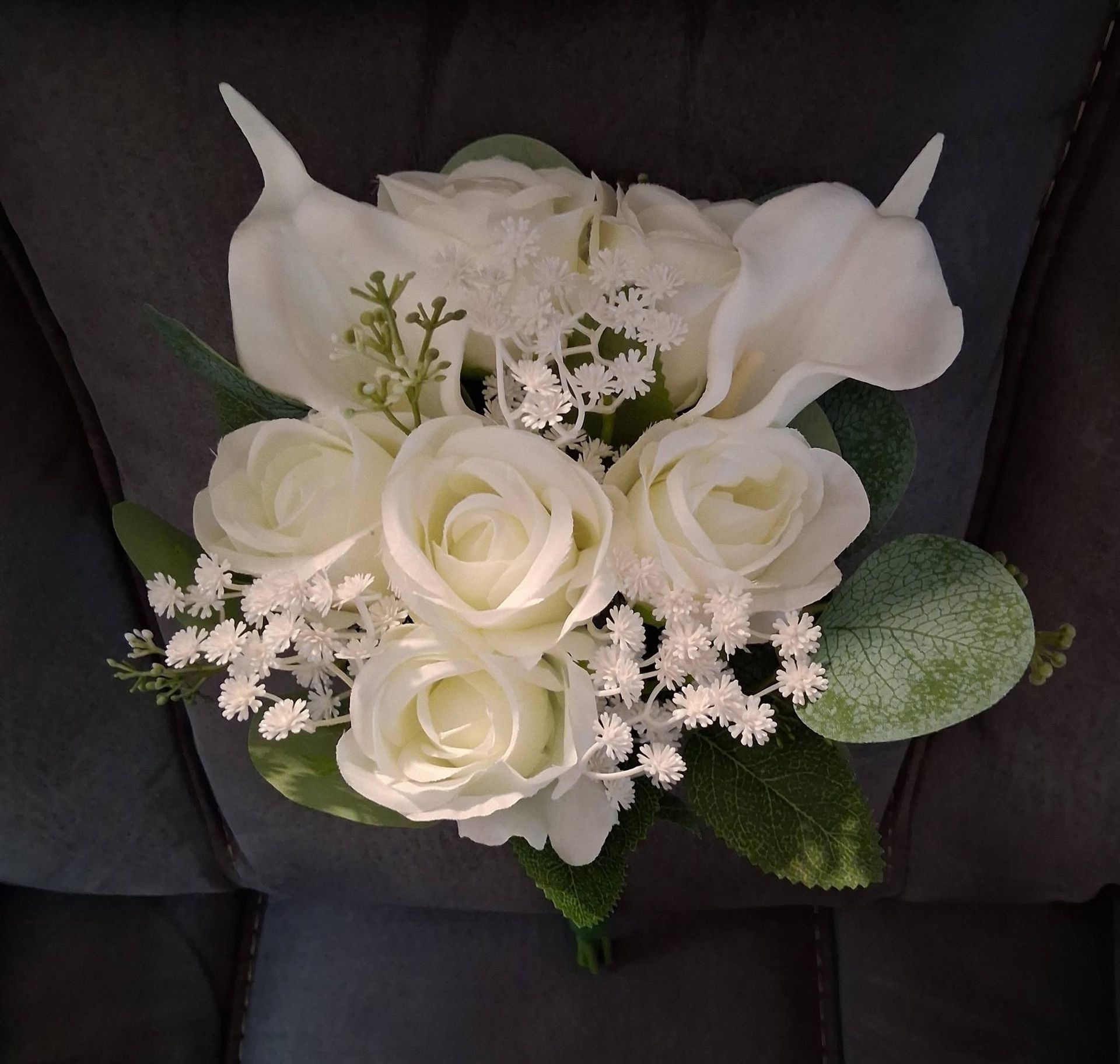 White rose bouquet with baby’s breath and green leaves on a dark background