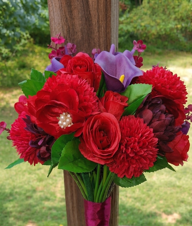 Red and purple flower bouquet in a vase with green leaves outdoors.