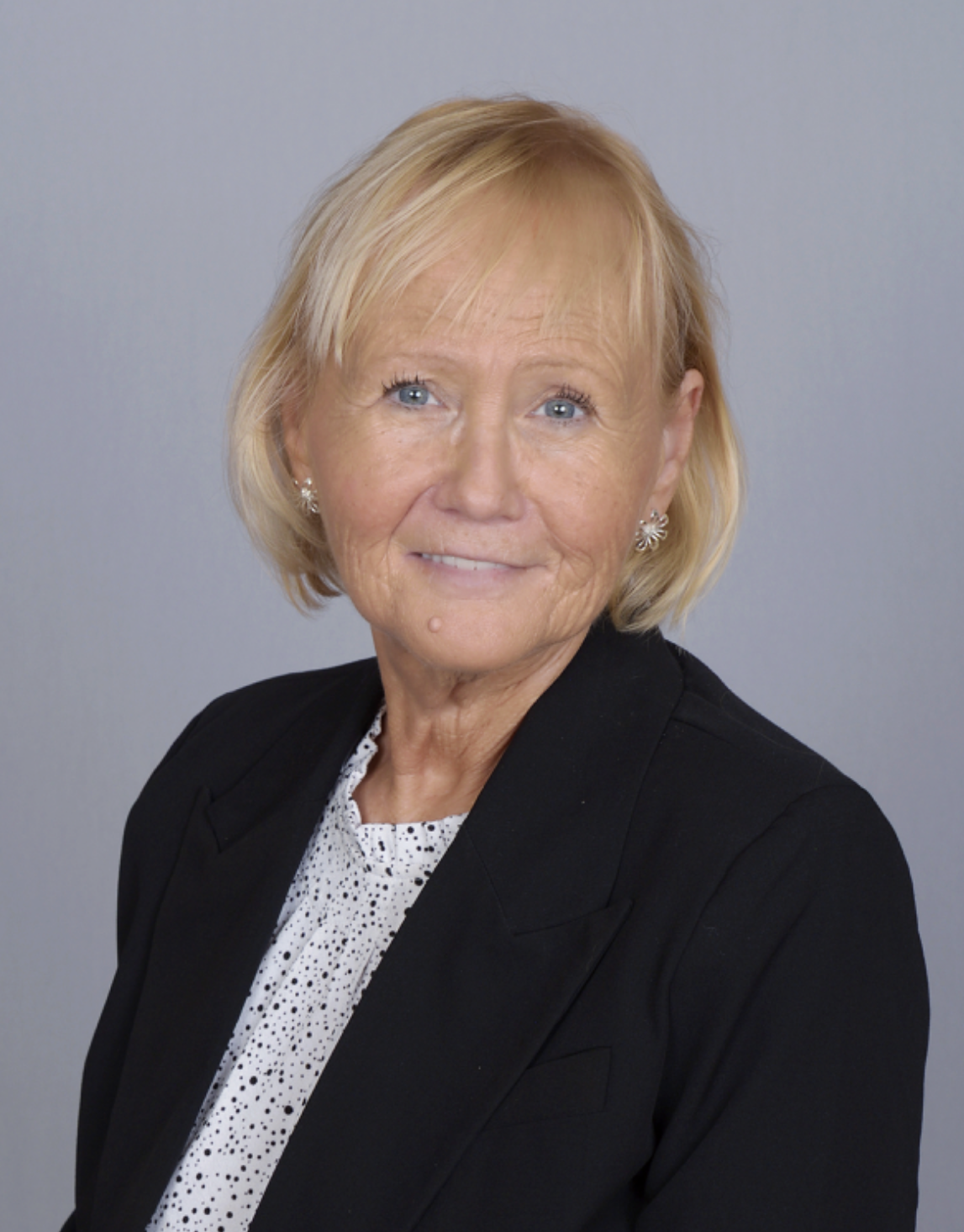 A woman in a black jacket and white polka dot shirt is smiling for the camera.
