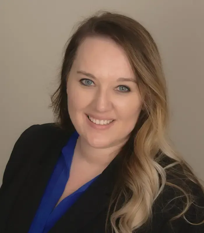 A woman in a blue shirt and black jacket is smiling for the camera.