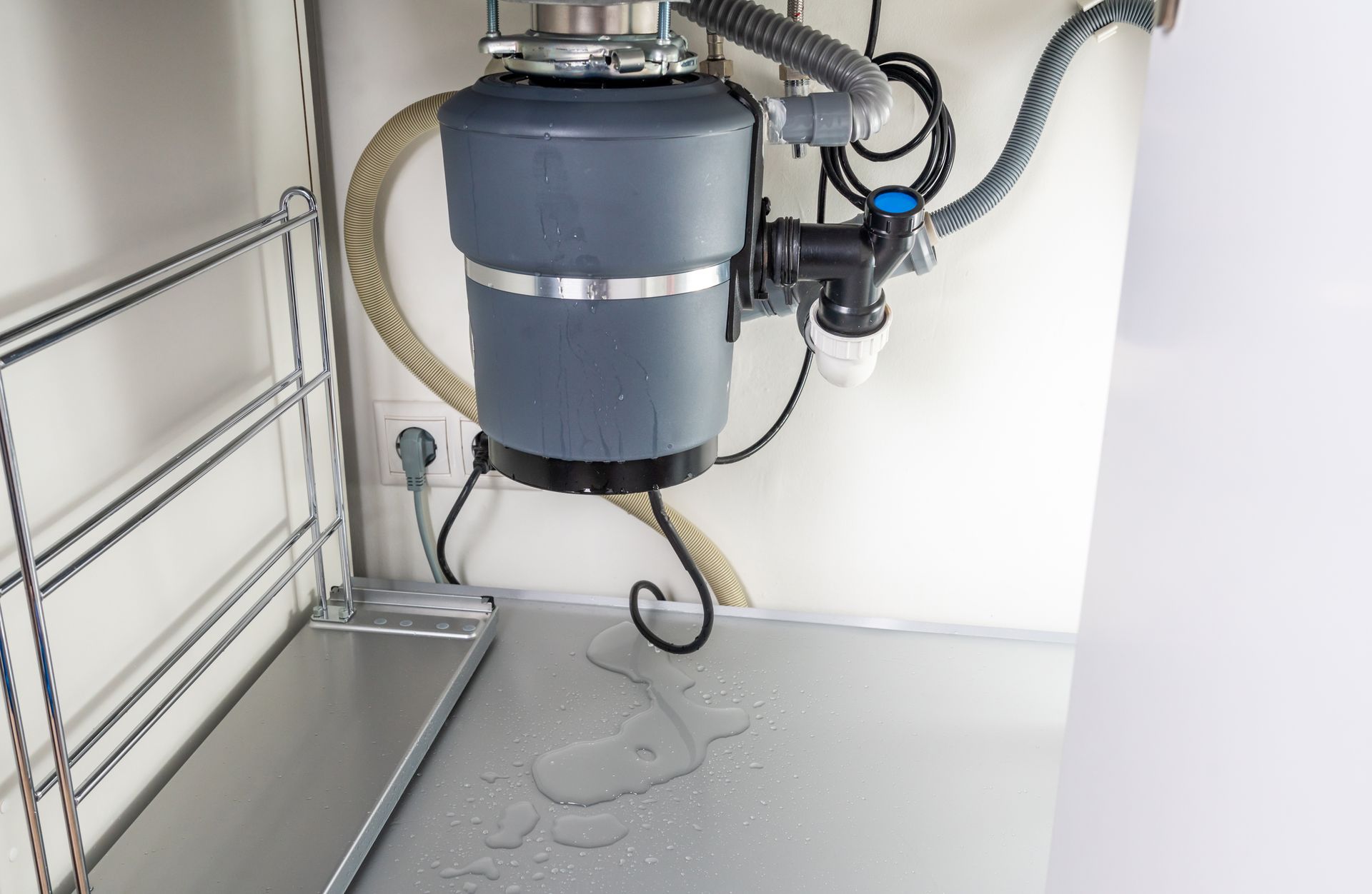 Blue industrial vacuum unit mounted on a wall in a utility room with hoses and a metal rack nearby