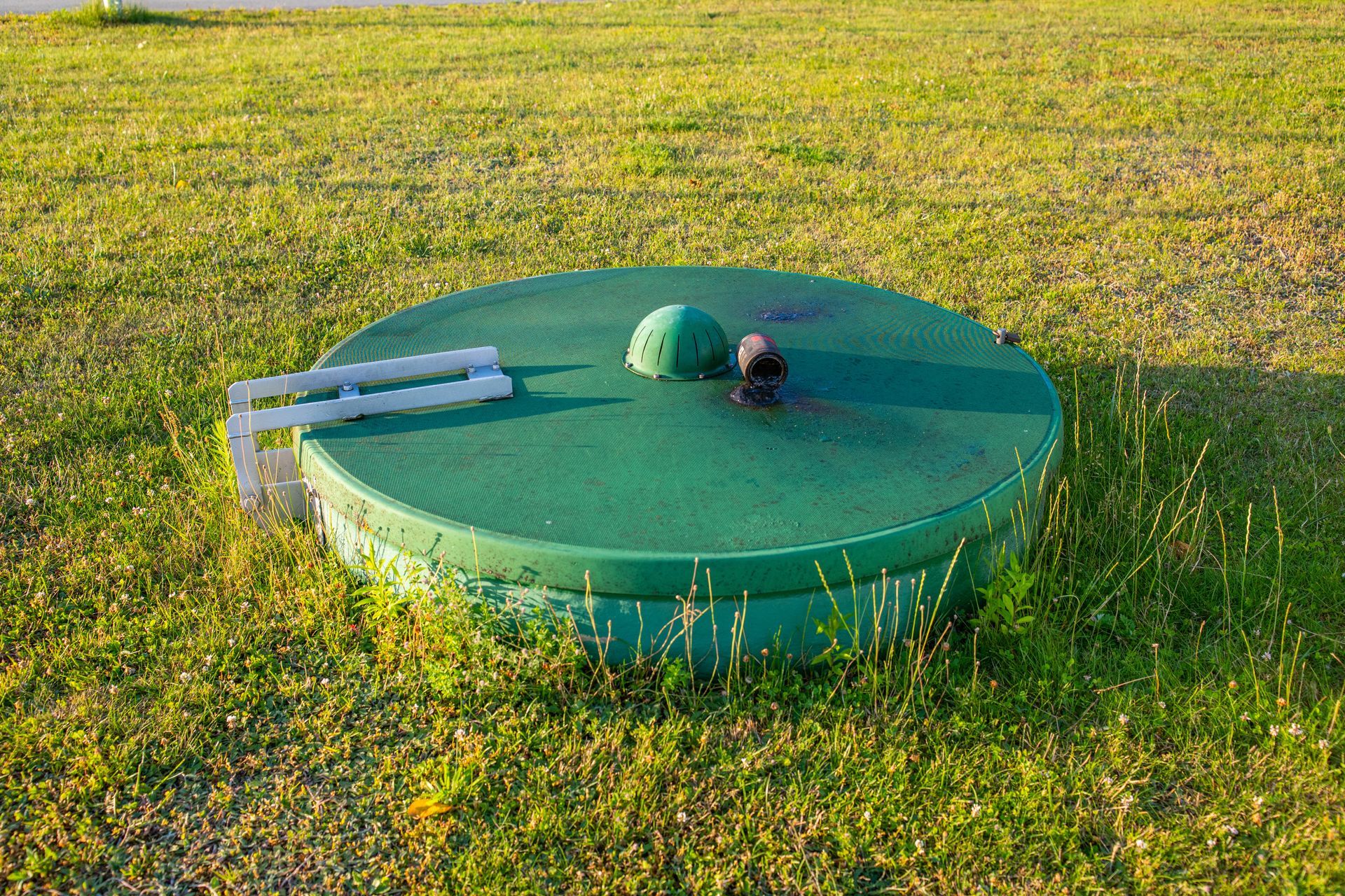 Green circular utility cover in grass with a metal handle attached on the left