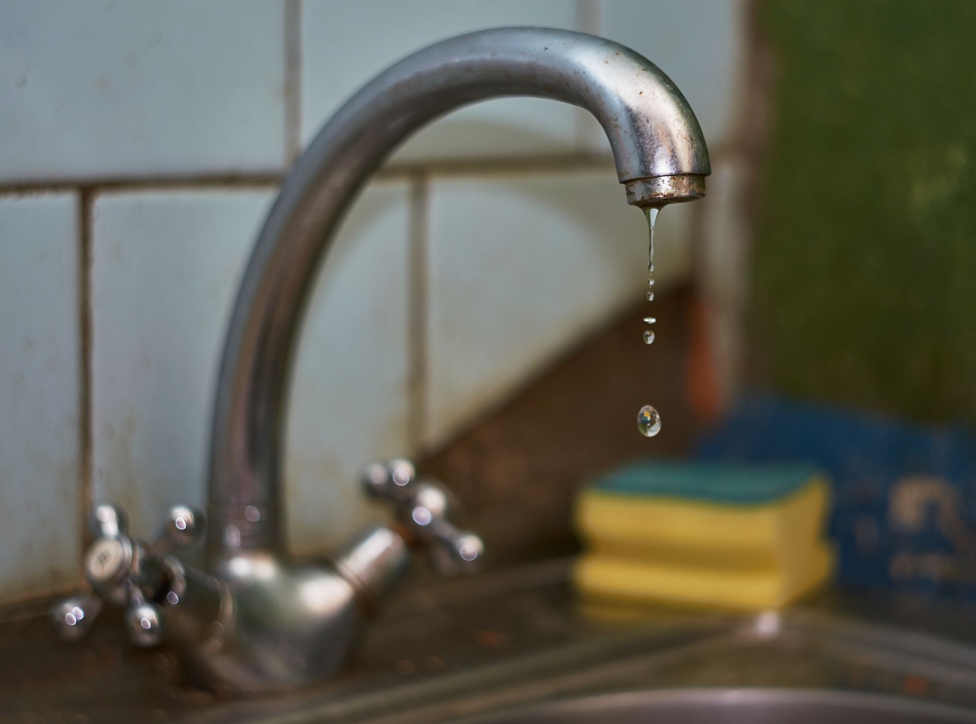Dripping kitchen faucet over a sink with a yellow sponge and blue cloth nearby