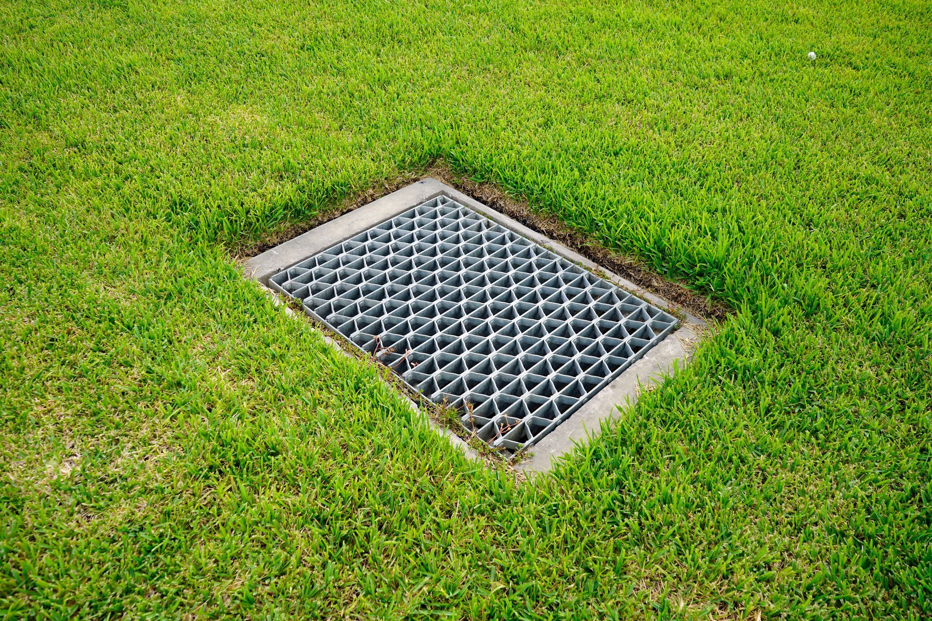 Metal drainage grate set in green grass lawn