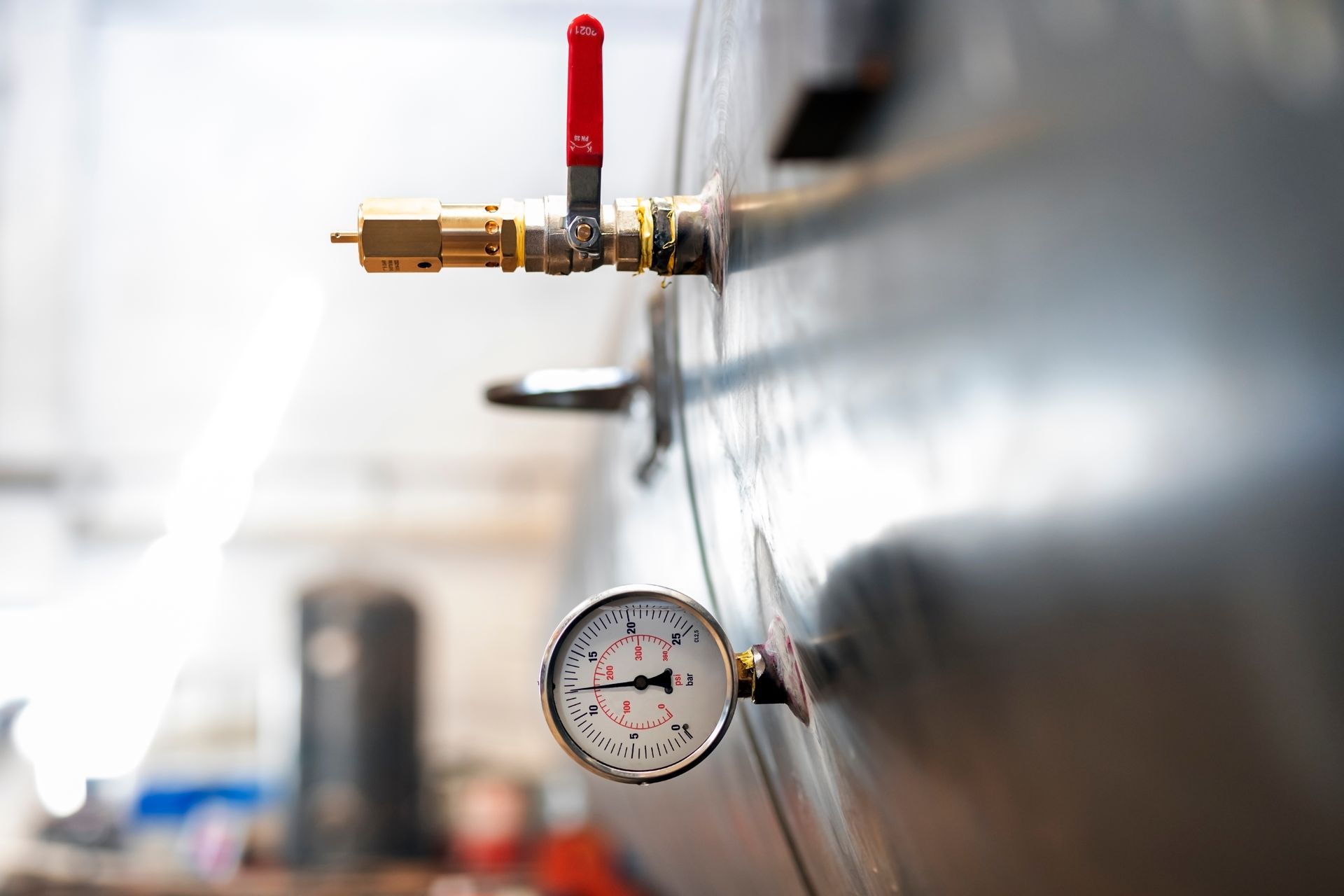 Pressure gauge and red-handled valve on a metal pipe in an industrial setting