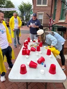 People in casual clothing play a game with red plastic cups on a folding table on an outdoor brick patio.
