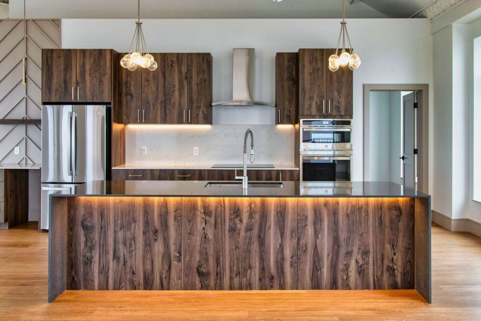 Modern kitchen with dark wood cabinets, stainless steel appliances, a large waterfall island, and warm under-cabinet lighting.