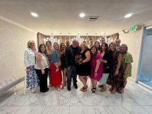A group of people standing in a bright, modern room with marble floors, posing together for a photo in front of curtains.