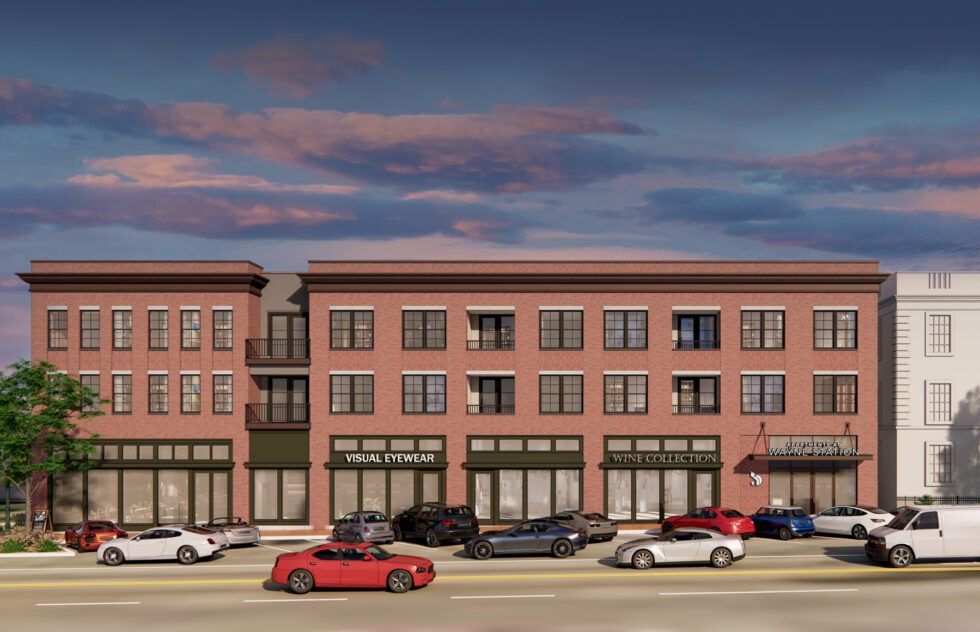 A three-story red brick commercial building with street-level storefronts, large windows, and parked cars in front.