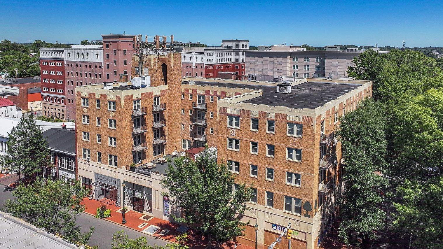 Brick apartment buildings beside a tree-lined street under a clear blue sky