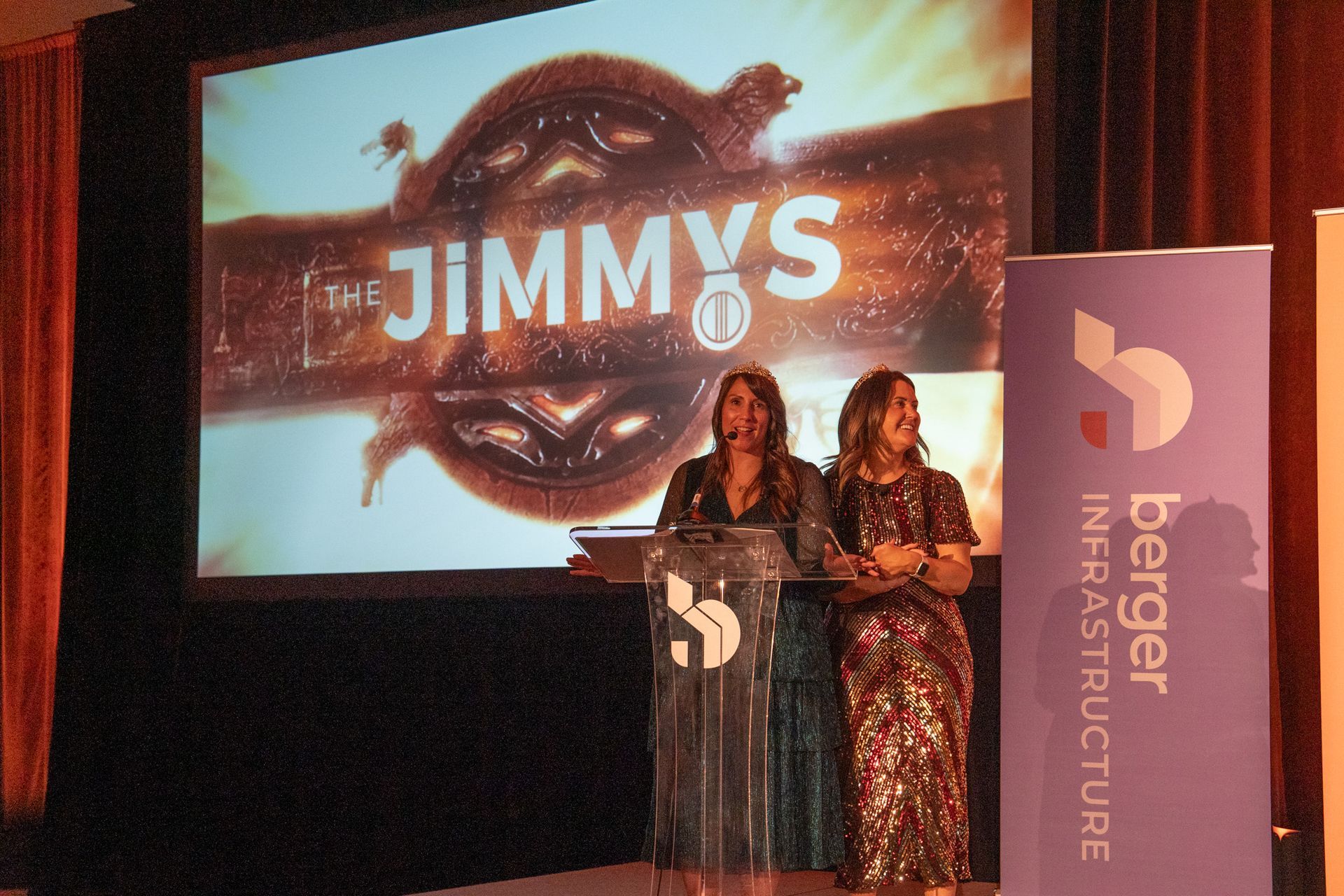Two people stand at a podium on stage under a "The Jimmys" screen, beside a purple Berger Infrastructure banner.