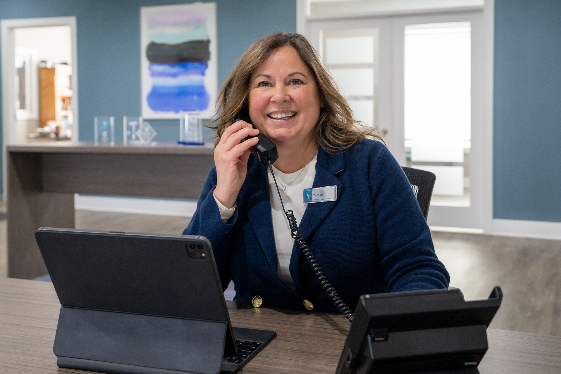 Smiling woman in a blue blazer sitting at a desk with a laptop in a bright office
